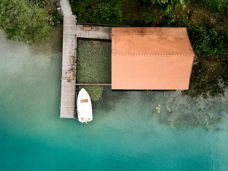 Aerial view of a boat docked at a wooden pier next to a boathouse on turquoise lake