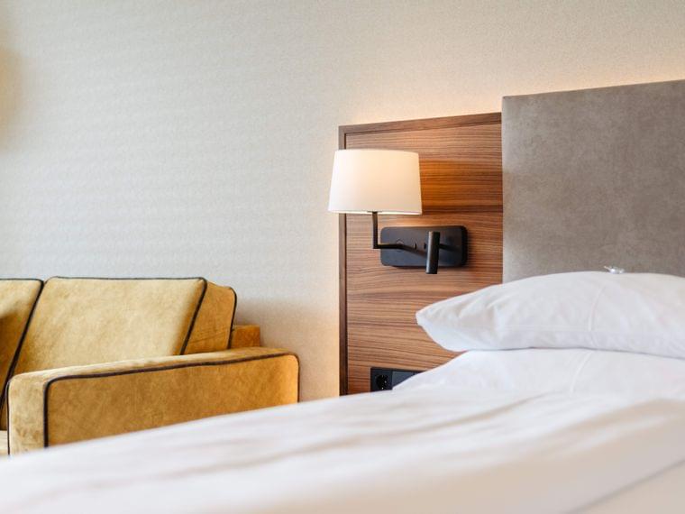 Modernes Hotelzimmer mit beigefarbendem Sofa, Wandleuchte und ordentlich gemachtem Bett