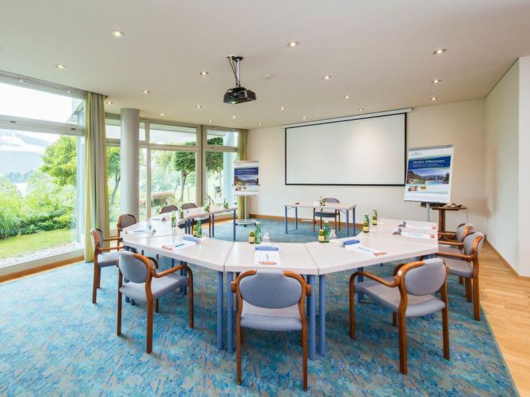 Sala conferenze luminosa con tavoli a U, proiettore e vista sul giardino