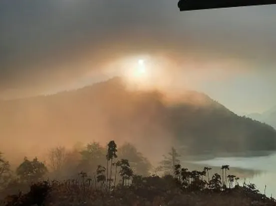 Sonnenaufgang über nebligem Berg mit Seeblick und Herbstbäumen im Vordergrund