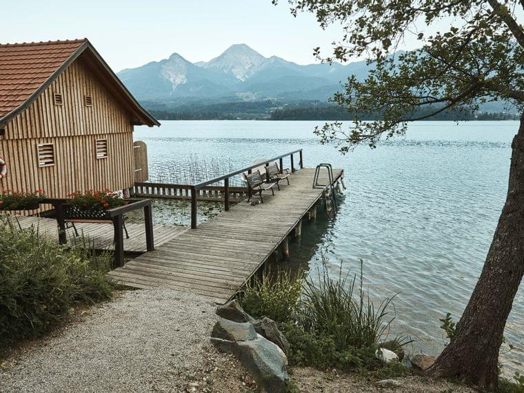 Holzbootshaus und Steg an ruhigem See mit Bergblick im Hintergrund