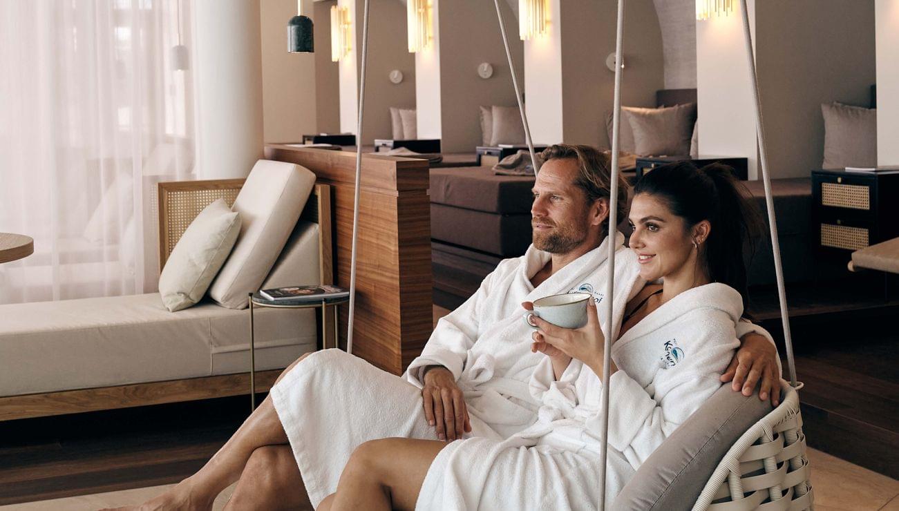 Coppia che si rilassa nella lounge della spa su una sedia sospesa con accappatoi bianchi