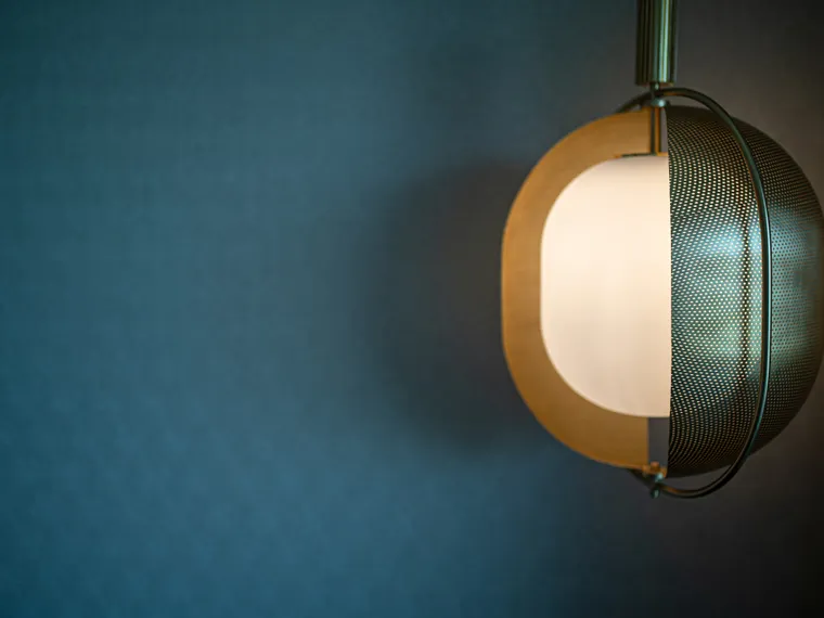 Moderne Pendelleuchte mit gelochtem Metallschirm vor dunkelblauer Strukturwand