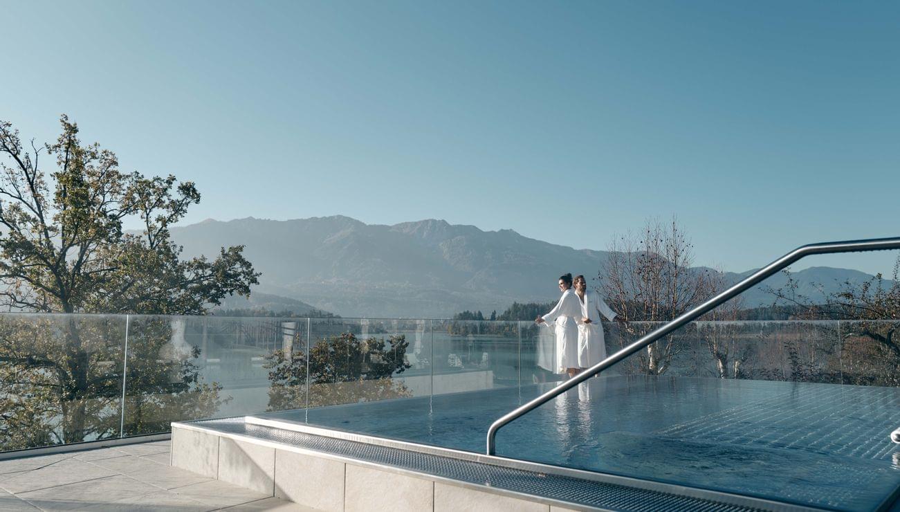 Paar im Bademantel am Infinity-Pool mit Blick auf See und Berge in einem Luxus-Wellnessresort