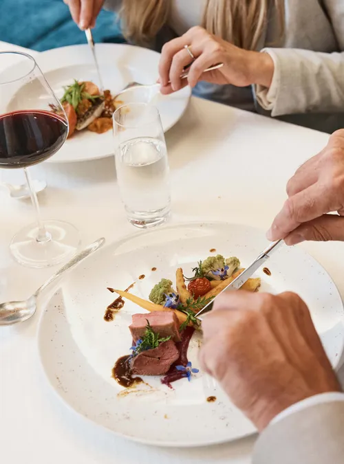 Elegantes Paar beim Essen mit Gourmet-Fleischgericht, Rotwein und edlem Tischgedeck