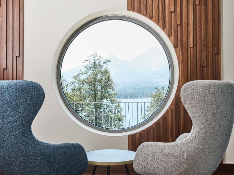 Moderne Loungesessel vor rundem Fenster mit Blick auf See und Berge