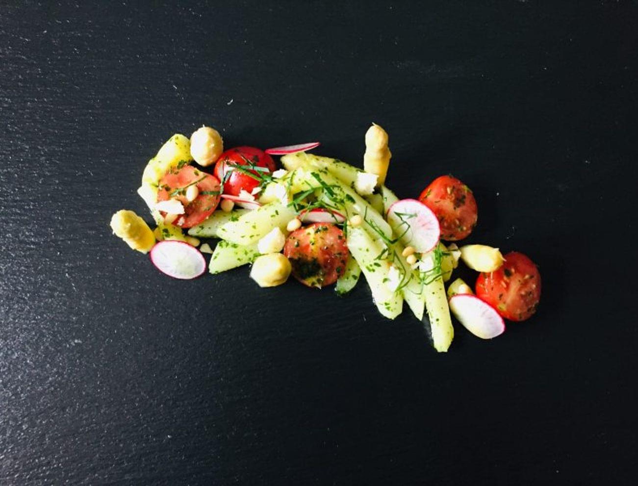 Gourmet-Kartoffelsalat mit Cherrytomaten, Radieschen und weißem Spargel auf schwarzem Schiefer