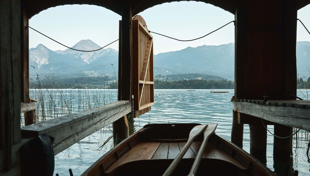 Barca a remi in legno in rimessa con vista sul lago di montagna attraverso il cancello aperto