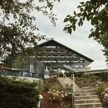 Hotel alpino con balconi in legno immerso in un giardino curato con scalini in pietra e fiori in fiore