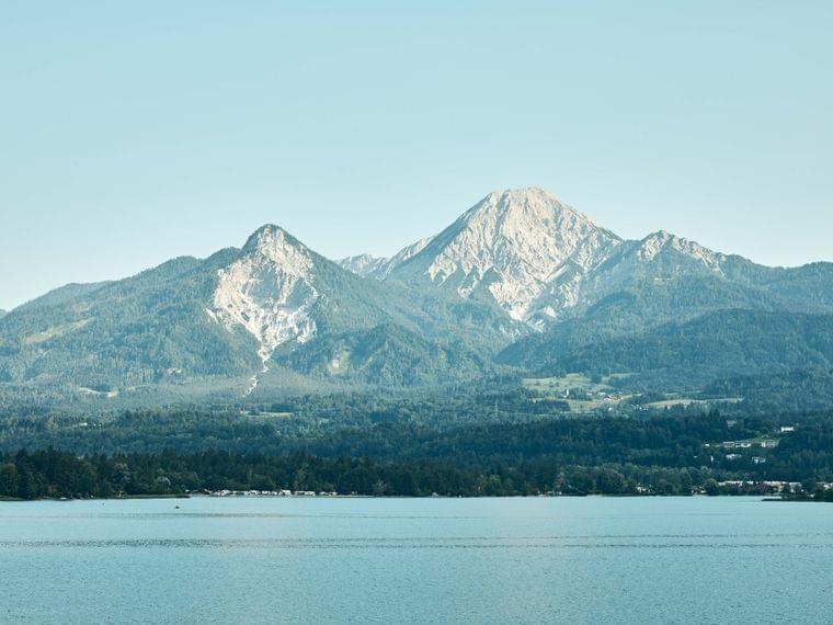 Mountain range with forest and lake in foreground under clear blue sky