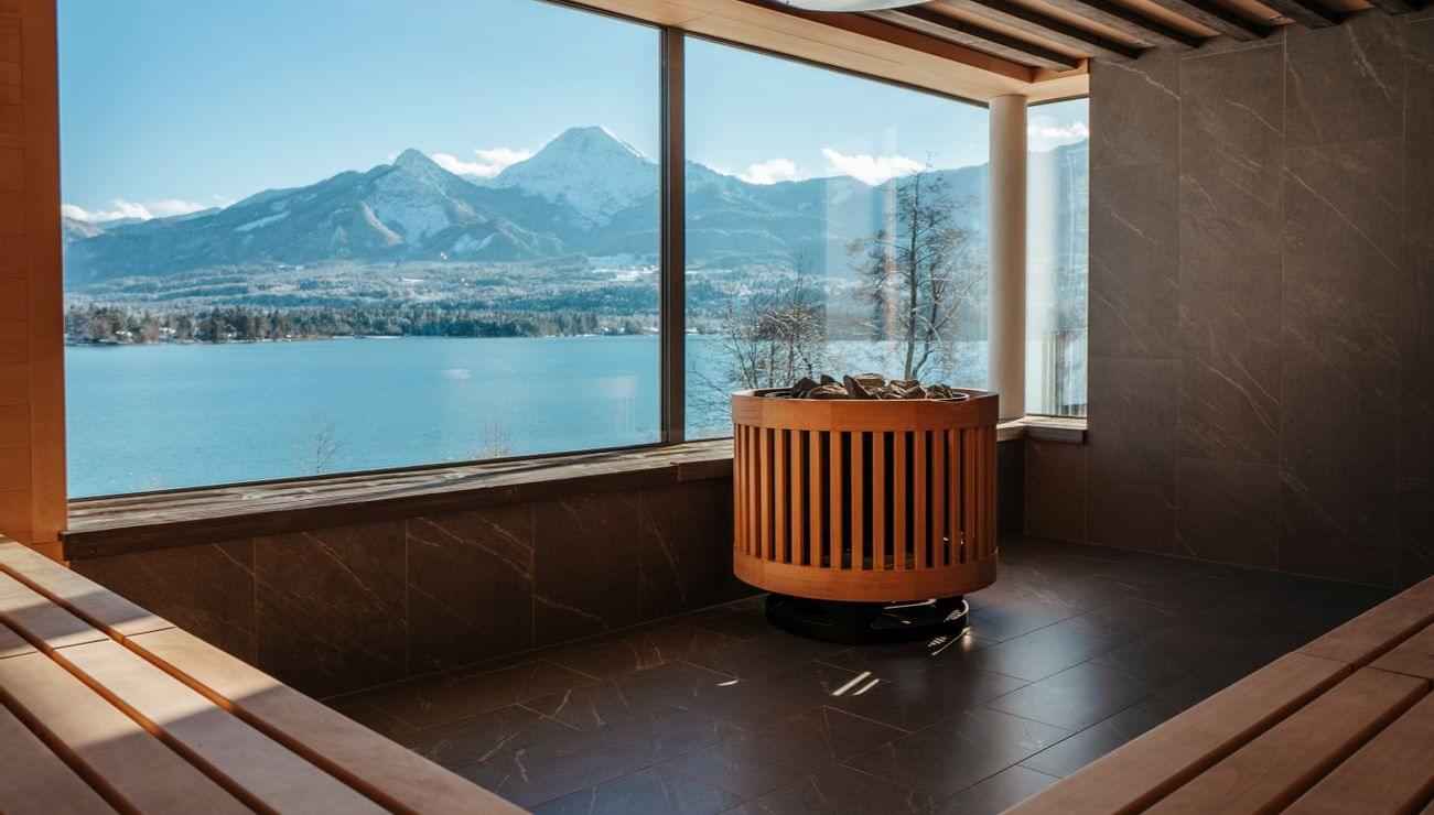 Sauna moderna con vista panoramica su lago alpino e montagne innevate