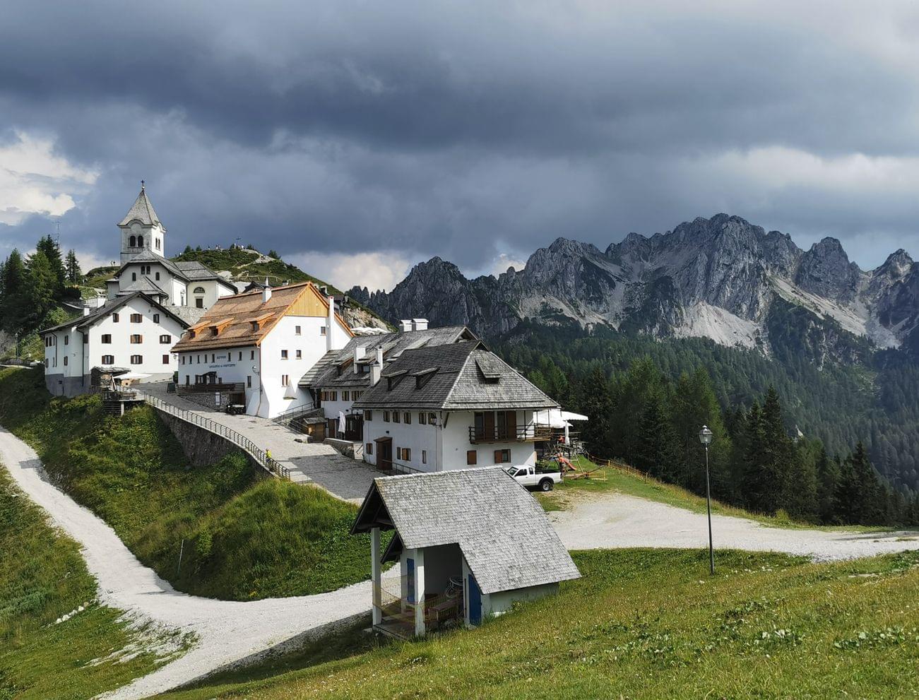 Bergdorf mit weißer Alpenkirche und Häusern unter dramatischem Wolkenhimmel