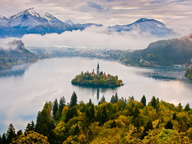 Lago di Bled con chiesa sull'isola, circondato da boschi autunnali e Alpi Giulie innevate