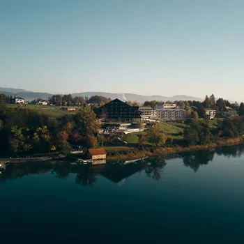 Seeufer-Resort mit bewaldeten Hügeln und ruhigem Wasser, das Gebäude und Herbstbäume spiegelt