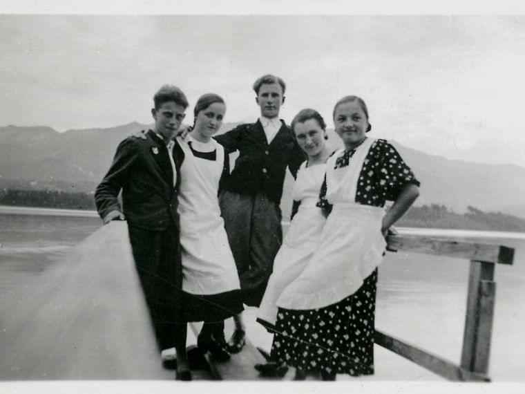 Vintage photo of five young adults in traditional attire standing on a lakeside pier