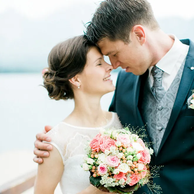 Sposa e sposo si abbracciano con un bouquet di rose pastello vicino all'acqua