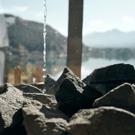 Wassertropfen auf heiße Saunasteine mit Bergen und See im Hintergrund