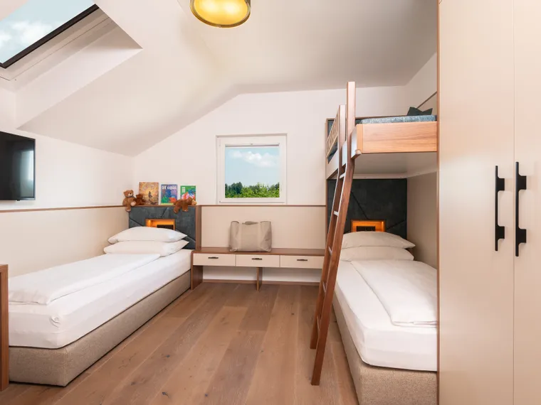 Modernes Familienzimmer mit zwei Einzelbetten und einem Etagenbett unter Dachfenster