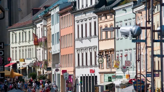 Belebte Einkaufsstraße mit bunten historischen Gebäuden und Ladenschildern in einer europäischen Stadt