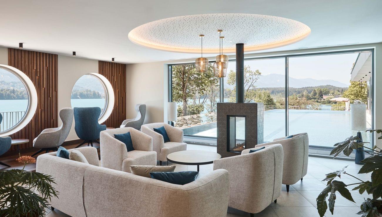 Moderne Hotellounge mit Panoramablick auf den See, gemütlichen Sesseln und Kamin am Infinity-Pool