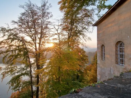 Historisches Gebäude mit Blick auf herbstlichen Wald und See bei Sonnenaufgang