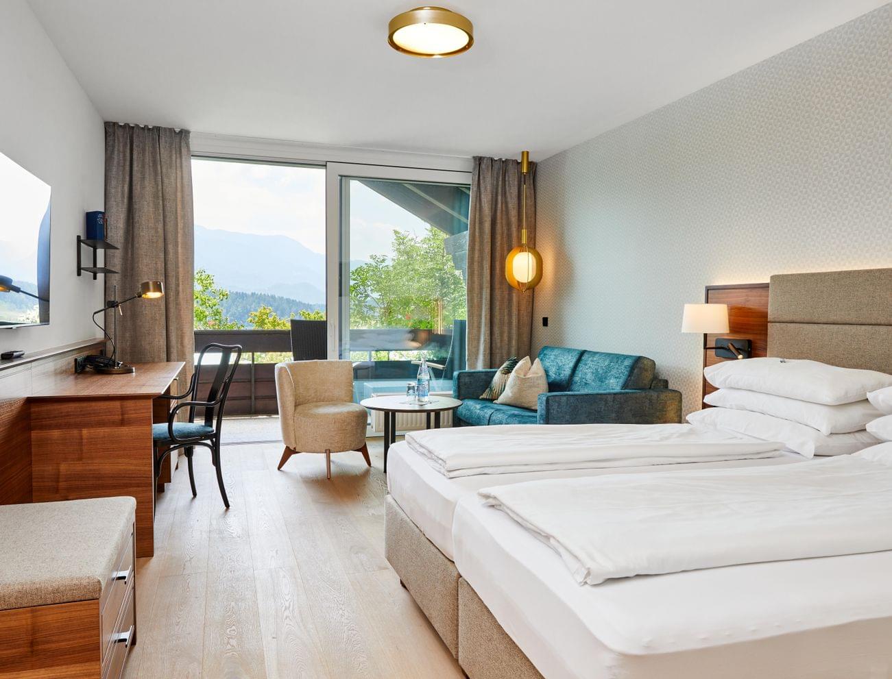 Modernes Hotelzimmer mit Doppelbett, Schreibtisch, Sitzecke und Balkon mit Bergblick