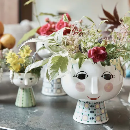 Dekorative keramikvasen mit Gesichtern und bunten Blumen auf einem Marmortisch