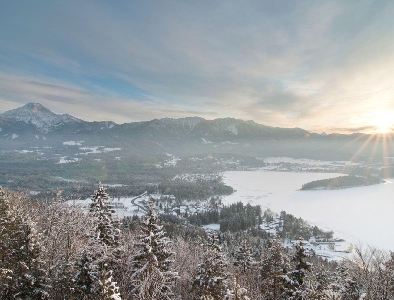 Verschneiter Wald und zugefrorener See bei Sonnenaufgang in den österreichischen Alpen