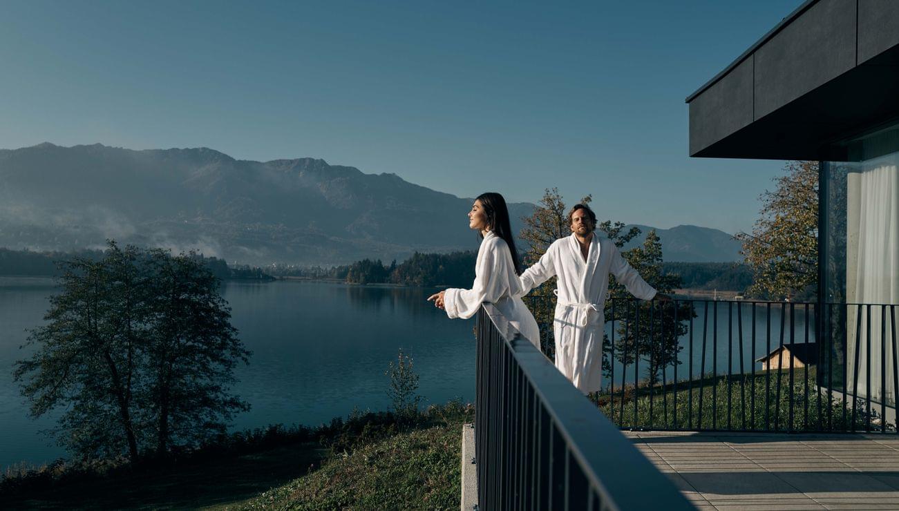 Coppia in accappatoi si gode la vista su lago e montagne dalla terrazza di un hotel spa