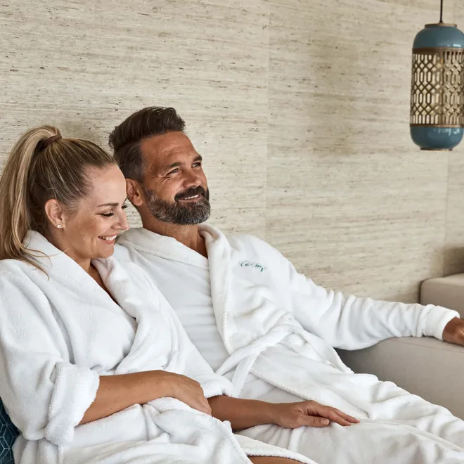 Smiling couple in white bathrobes relaxing on a spa lounge sofa