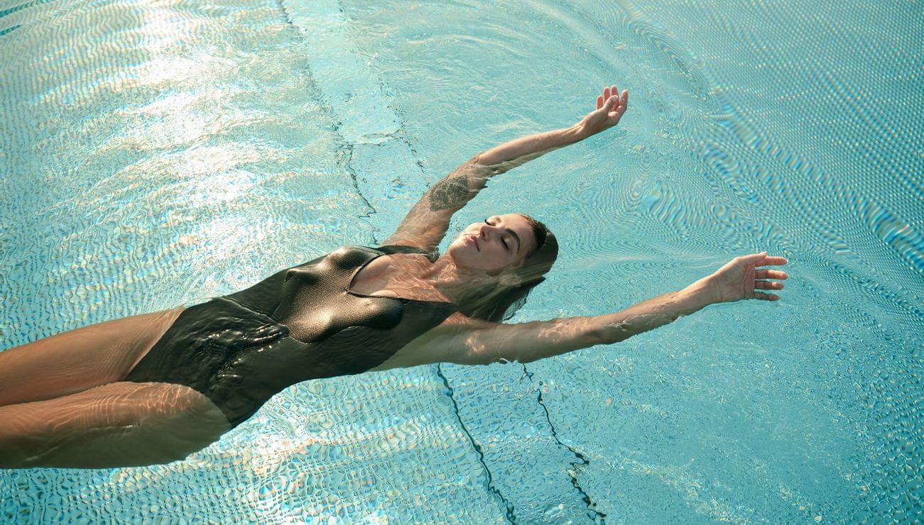Frau im schwarzen Badeanzug treibt rücklings in einem klaren blauen Schwimmbecken