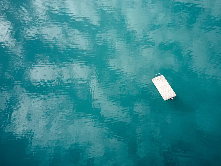 Schwimmender Holzsteg auf ruhigem türkisfarbenem See mit Himmelsreflexionen