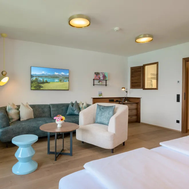 Modernes Hotelzimmer mit Sofa, Sessel, Schreibtisch, Fernseher und Holzfußboden