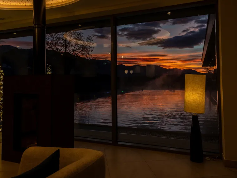 Gemütliche Lounge mit Kamin und Sonnenuntergangsblick über Infinity-Pool durch große Glasfront