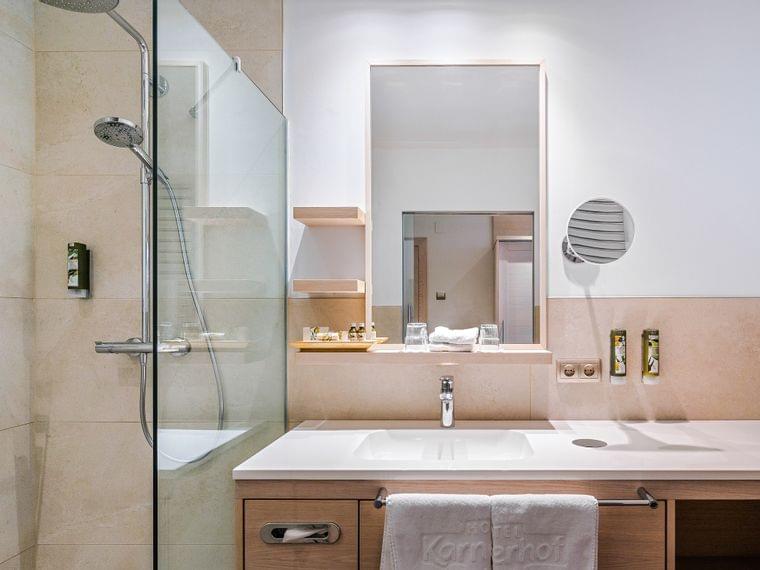 Modernes Hotelbad mit begehbarer Dusche, großem Spiegel und Holzwaschtisch