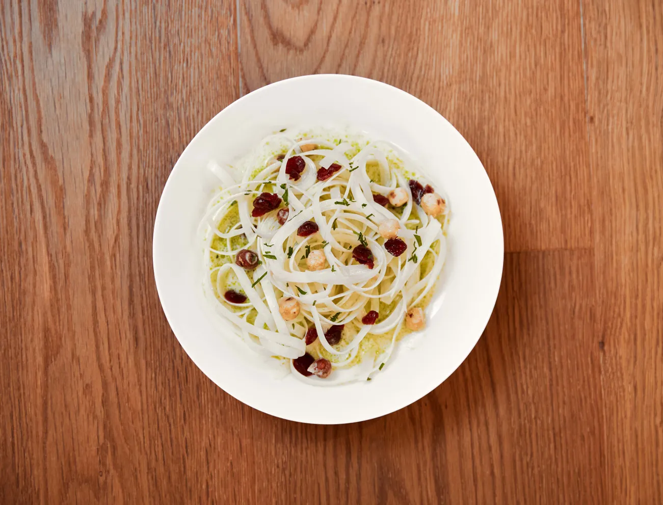White pasta with pesto sauce, cranberries, and hazelnuts in a white bowl on wooden table