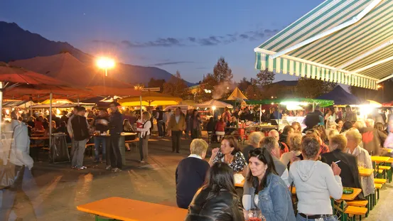 Belebter nächtlicher Freiluftmarkt mit Essensständen und Menschen an langen Bänken