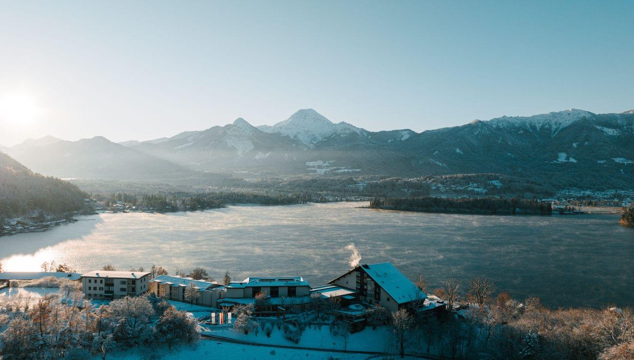 Villaggio innevato sul lago con montagne alpine e alba in paesaggio invernale