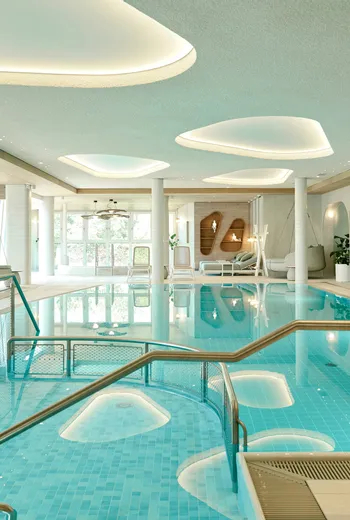 Modernes Hotelhallenbad mit Liegestühlen und eleganter Deckenbeleuchtung