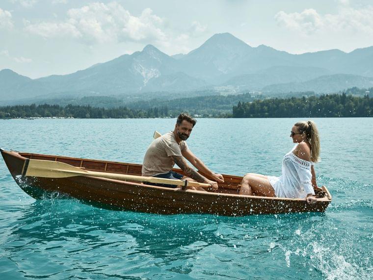 Couple rowing wooden boat on turquoise lake with mountains in the background