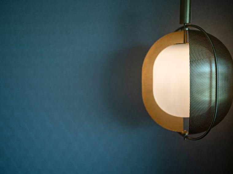 Moderne Pendelleuchte mit gelochtem Metallschirm vor dunkelblauer Strukturwand
