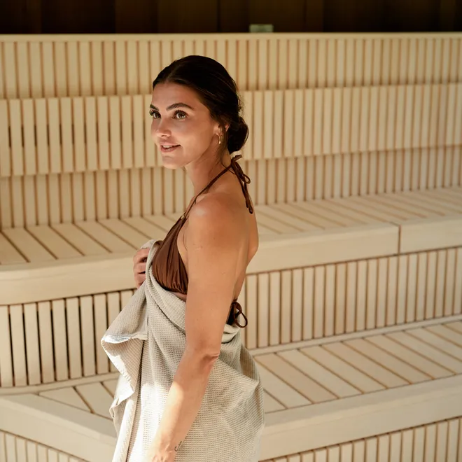 Frau im Badeanzug mit Handtuch steht in moderner Holzsauna