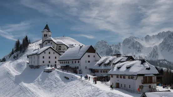 Schneebedecktes Alpendorf mit Kirche und Skifahrern in den Dolomiten