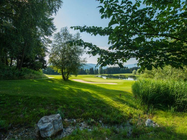Grüner Golfplatz mit Sandbunker, Bäumen und See unter klarem blauen Himmel
