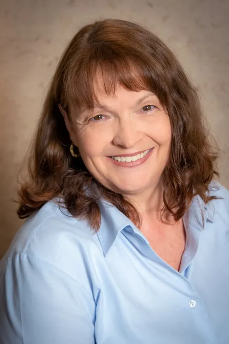 Smiling middle-aged woman with wavy brown hair wearing a light blue shirt