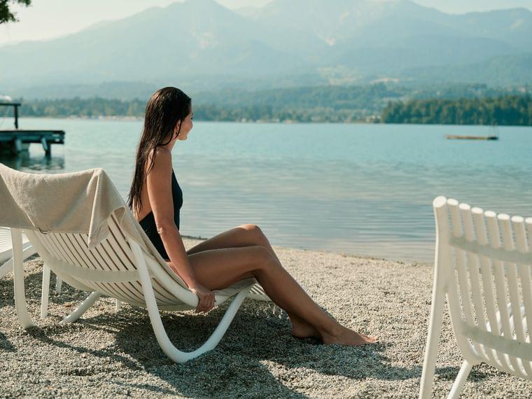 Donna in costume nero rilassata sulla spiaggia del lago con vista sulle montagne