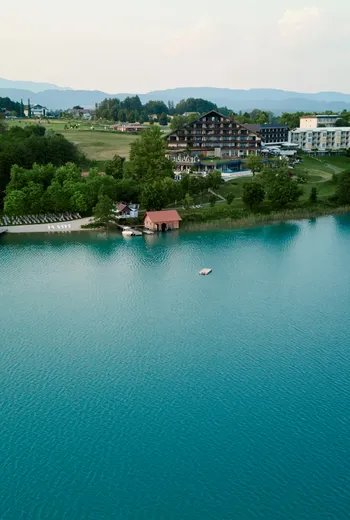 Resort sul lago con vegetazione rigogliosa e acqua blu limpida circondato da montagne
