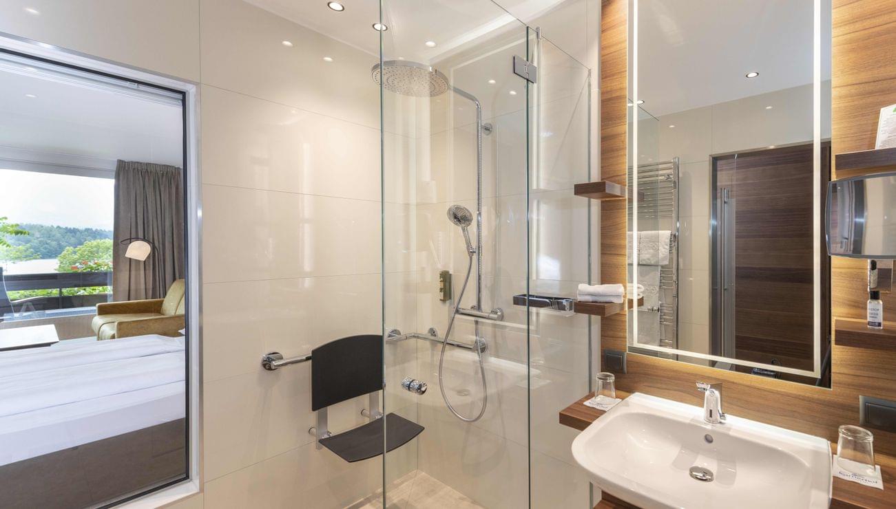 Modern hotel bathroom with accessible shower chair and large illuminated mirror