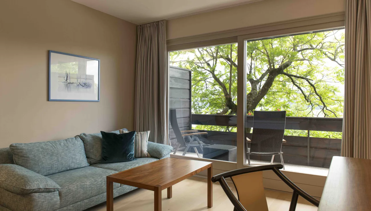 Modernes Wohnzimmer mit Sofa und Holztisch mit Blick auf Balkon und Bäume