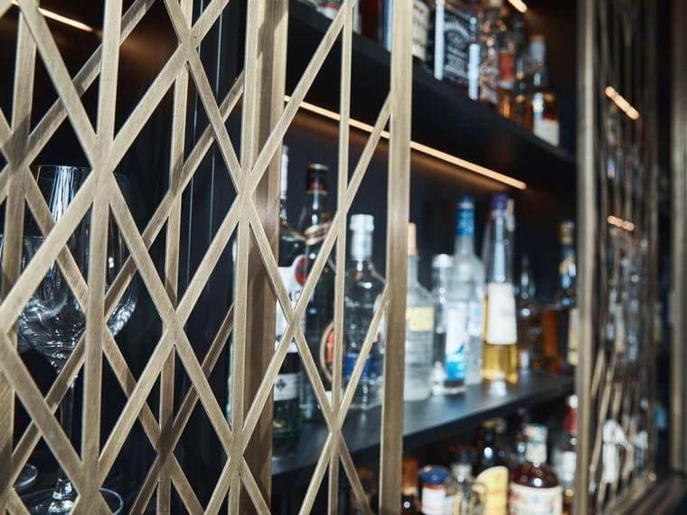 Modern liquor shelf with various alcohol bottles behind decorative metal lattice